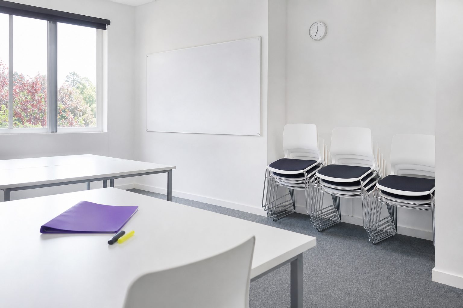 A nearly empty tutoring room with chairs stacked against a white wall and one violet folder left behind