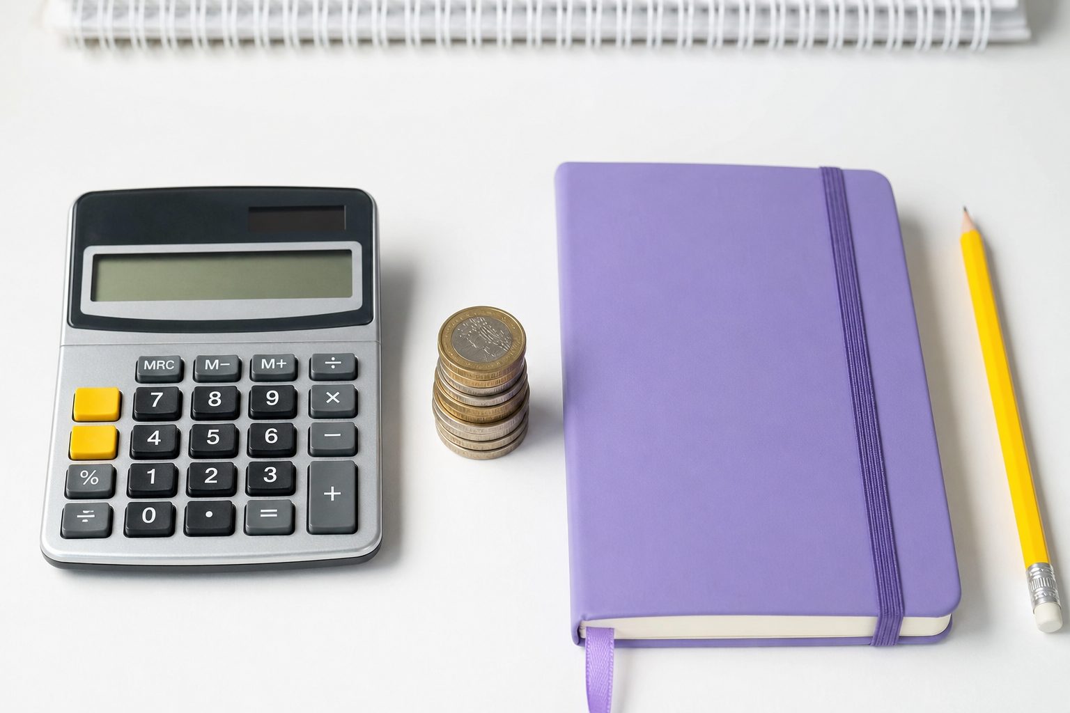 A calculator, stack of coins, violet notebook and yellow pencil lined up on a white desk surface